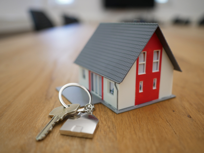 A close-up of a set of house keys next to a miniature house. 